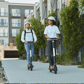 A stylish couple, a handsome man and an attractive woman, ride the Hoverfly GXL MAX Electric Scooter effortlessly through the bustling city streets, demonstrating the scooter's convenience and comfort for urban commuting