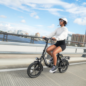 Girl Enjoying Urban Ride on Black Hoverfly H3 Foldable E-Bike, Skyline & Blue Skies in View.